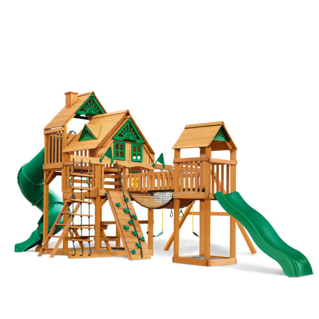 The Gorilla Playsets Treasure Trove II Treehouse Wooden Swing Set is a large wooden set featuring two elevated playhouses, green slides, ladders, a rock climbing wall, and a rope bridge with green accents on white.