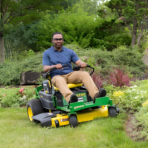 Man operating a John Deere zero-turn mower on a green lawn